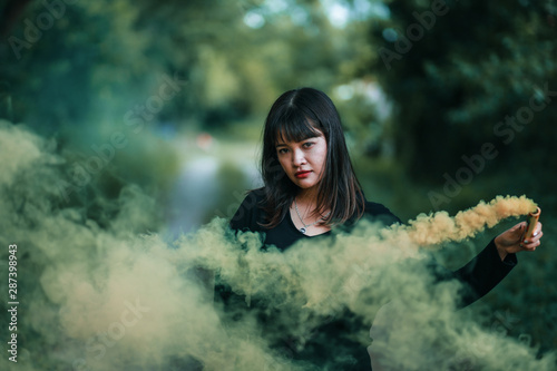 Fototapeta Naklejka Na Ścianę i Meble -  Portrait of Asian woman in black cloth with color fire smoke in forest witch concept