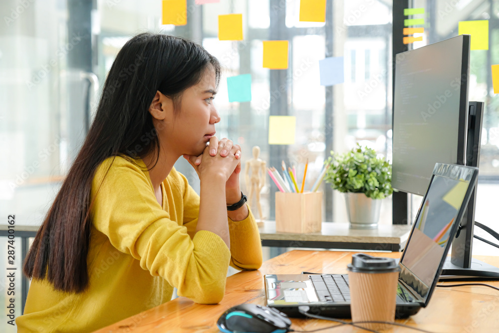Asian female programmer for yellow shirt sitting with a hand on her chin,She stared at the computer screen and pondered. Asian female programmer for yellow shirt sitting with a hand on her chin,She stared at the computer screen and pondered.