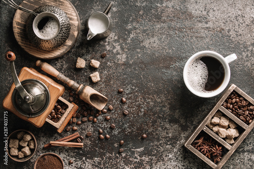 Coffee cup with coffee grinder and coffee beans on dark textured background.