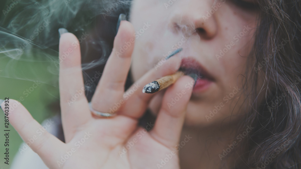 Obraz premium Girl smoking medical marijuana joint outdoors, close-up. Cannabis is a concept of herbal medicine.