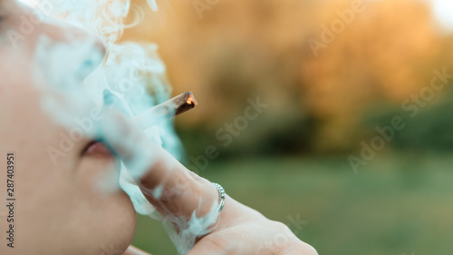 Girl smoking medical marijuana joint outdoors, close-up. Cannabis is a concept of herbal medicine.