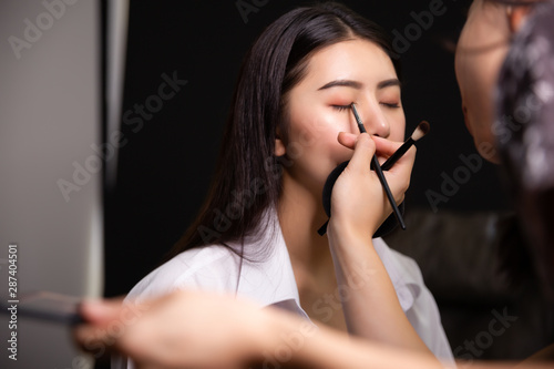 Beautiful young asian woman and professional makeup artists applies eye shadow. Beautiful woman face. Perfect makeup