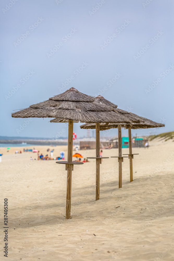 View of a beach with four straw parasol, summer weather with tourist people taking sunbathing