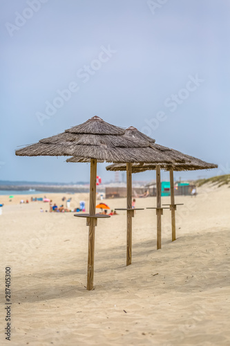 View of a beach with four straw parasol, summer weather with tourist people taking sunbathing © Miguel Almeida