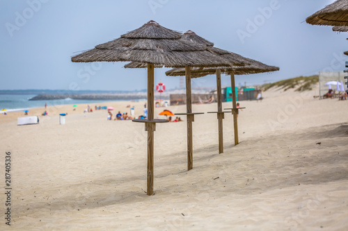 View of a beach with four straw parasol  summer weather with tourist people taking sunbathing