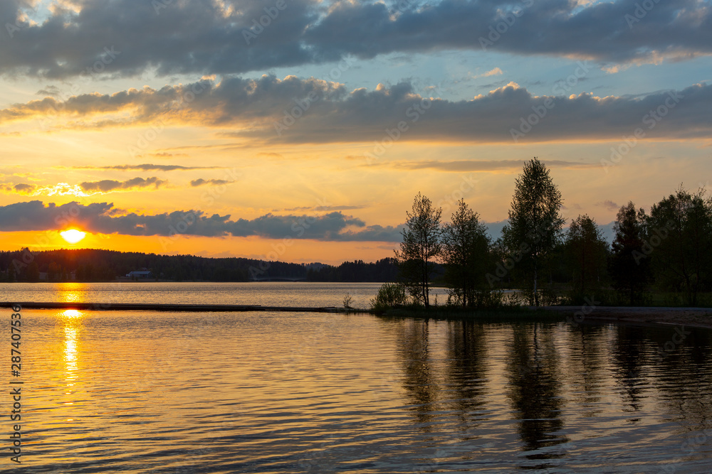 Amazing sunset in Finland during summer evening. Golden hour and dramatic clouds. Reflection in water, calm scenery.
