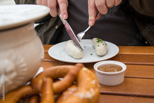 Mann isst Münchener Weißwurst mit Messer und Gabel, süßen Senf und Brezel und löst Wurst richtig aus Pelle draußen in Biergraten