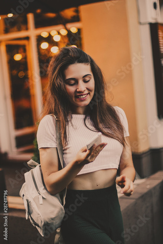 Smiling woman using phone and drink coffee on the street in summer day.