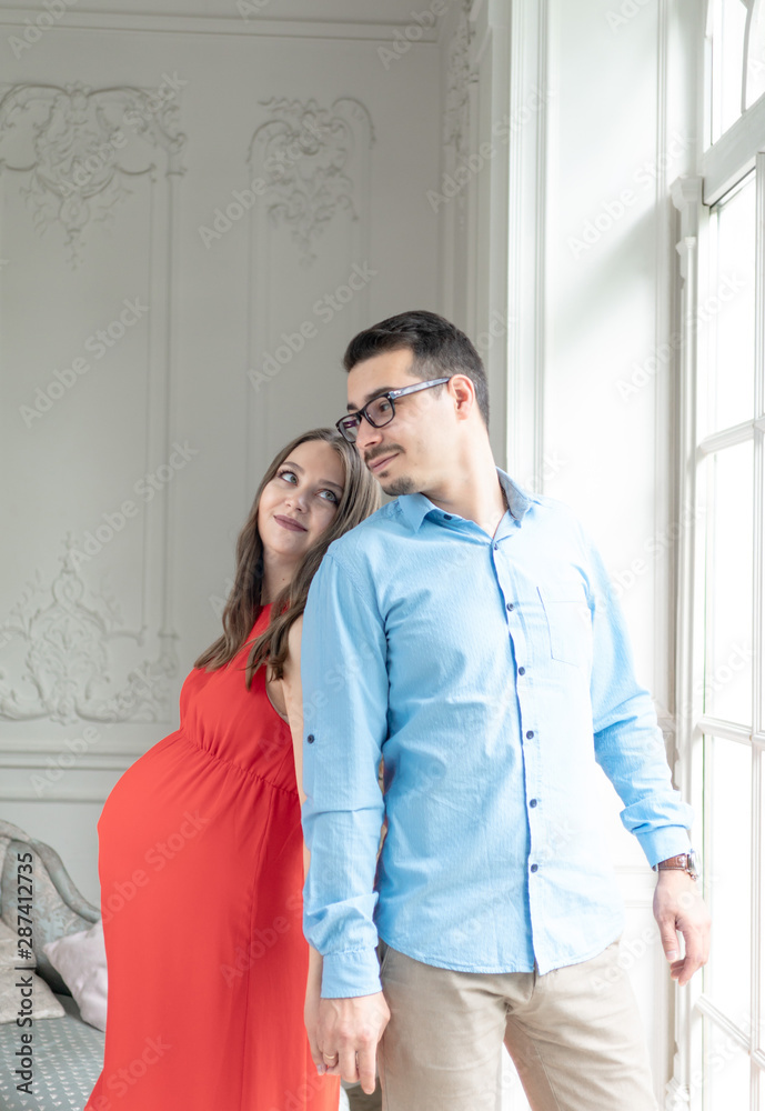 expectant parents waiting for their first child. a pregnant woman in a red dress with her husband. young parent expectant parents waiting for their first child. a pregnant woman in a red dress with her husband. young parent