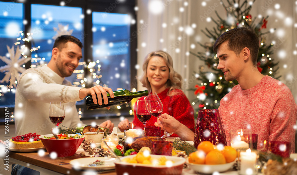 holidays and celebration concept - happy friends having christmas dinner at home and drinking red wine over snow