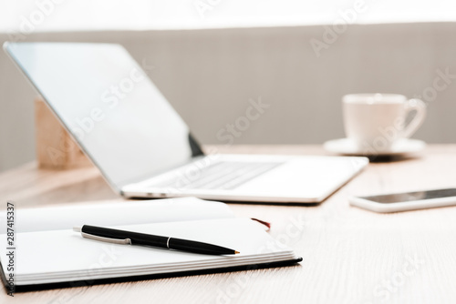 selective focus of notebook and pen near gadgets on table