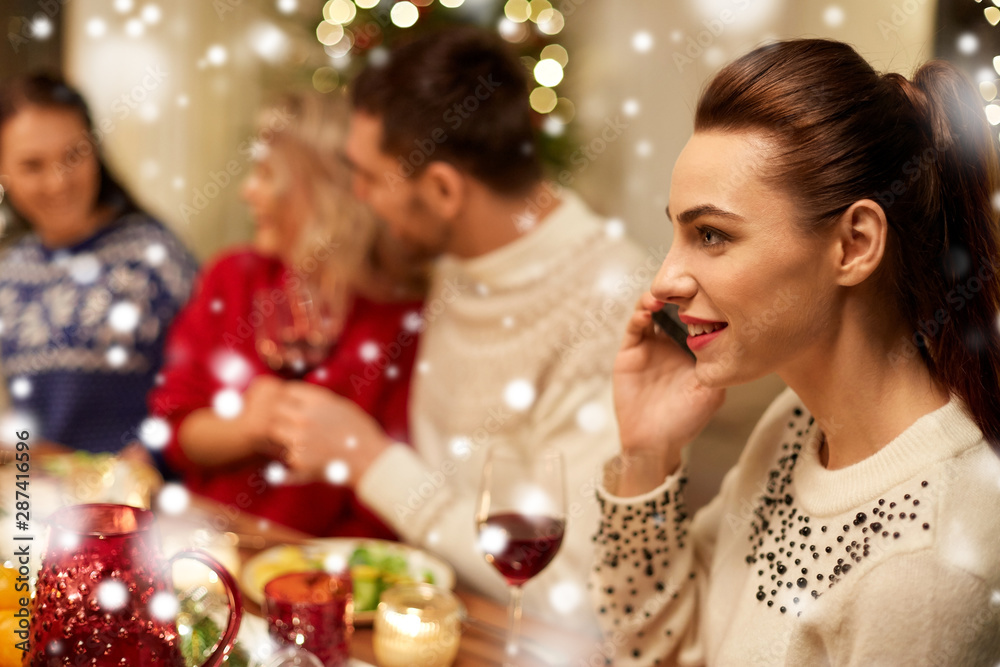 holidays, communication and celebration concept - close up of young woman calling on smartphone and having christmas dinner with friends at home over snow