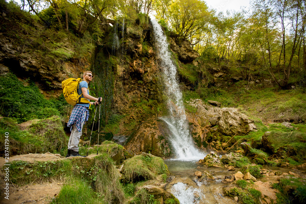 Young hiker stopped beside a mountain waterfall to rest Young hiker stopped beside a mountain waterfall to rest
