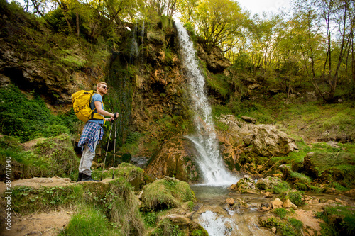 Young hiker stopped beside a mountain waterfall to rest