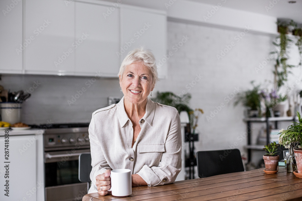 Portrait mature adult woman looking out of window with a mug of tea Portrait mature adult woman looking out of window with a mug of tea