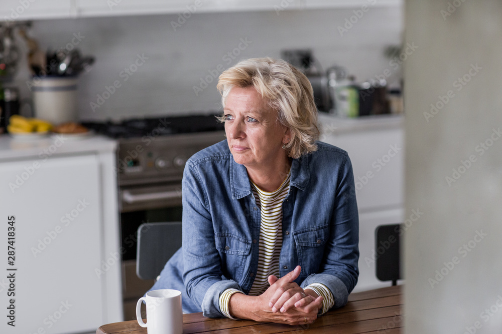 Mature adult woman looking out of window with a mug of tea Mature adult woman looking out of window with a mug of tea