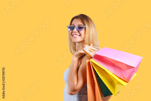 Black friday season sale concept. Attractive young woman with long blonde hair, wearing sexy tight dress, holding many different blank shopping bags, yellow isolated background. Copy space, close up