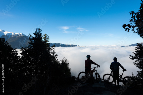 Mountain bikers look out across a valley filled with a cloud inversion in the Himalayas while biking in the Gosainkund region, Langtang region, Nepal photo