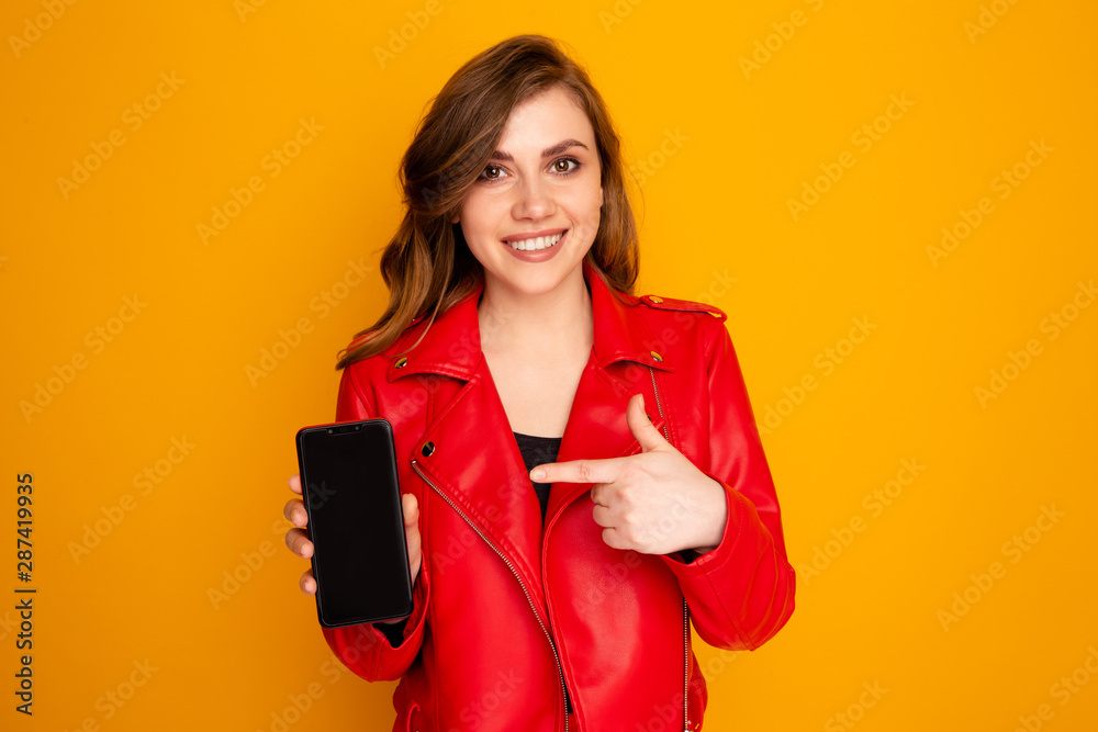 Closeup photo of girl pointing black phone isolated over the yellow background Closeup photo of girl pointing black phone isolated over the yellow background