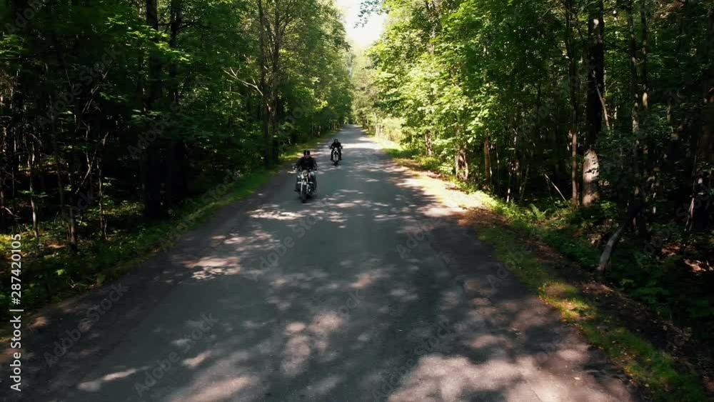 Two adult men motorcyclists in helmet riding a motorbike in the forest