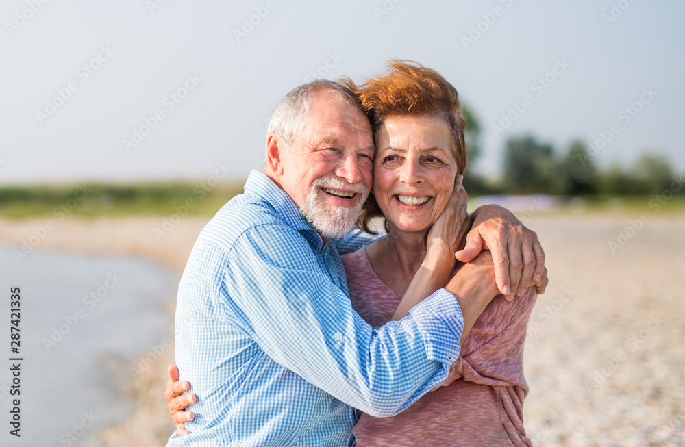 Senior couple on a holiday on a walk by the lake, hugging. - obrazy, fototapety, plakaty 