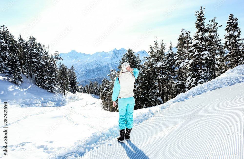 Girl in ski suit in winter in the mountains against the forest and mountain peaks