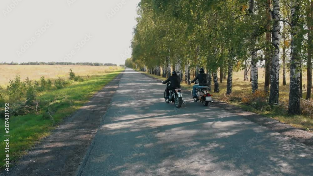Two men motorcyclists starts riding by the birch grove Two men motorcyclists starts riding by the birch grove