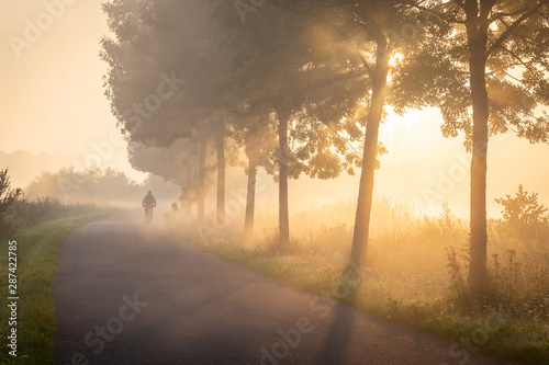 Cyclist in the fog on the towpath along the Lys in Lauwe - Menen, Belgium. After a cold and clear night we often get a layer of fog over the fields. This creates beautiful atmospheric pictures of the photo