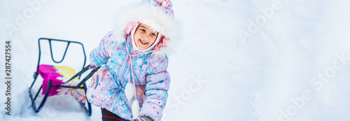 Pretty smiling little girl in her ski suit sliding down a small snow covered hill with her sledge board during a bright sunny winter day photo