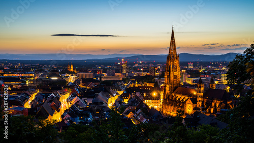 Germany, Freiburg im breisgau cityscape and minster or muenster cathedral in magical atmosphere after sunset in summer from famous square above the city