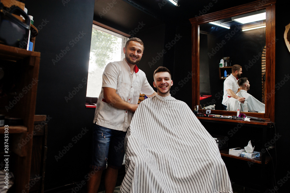 Young bearded man getting haircut by hairdresser while sitting in chair at barbershop. Barber soul. Young bearded man getting haircut by hairdresser while sitting in chair at barbershop. Barber soul.