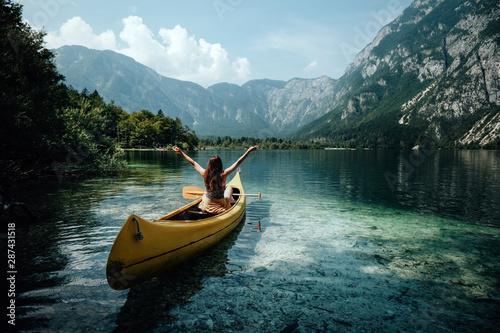Young woman canoeing in the lake bohinj on a summer day, background alps mountains.