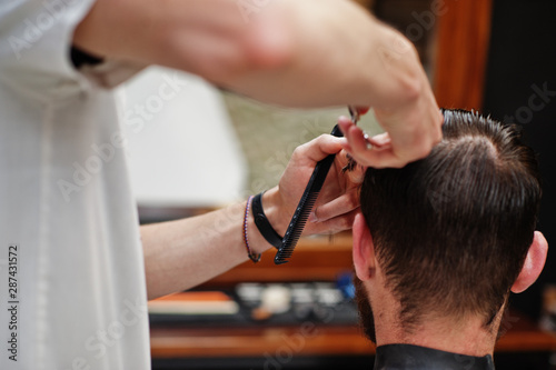 Young bearded man getting haircut by hairdresser while sitting in chair at barbershop. Barber soul. © AS Photo Family