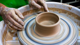 A raw clay pot in the hands of a potter. Workshop in the pottery workshop. Clay pot on a potter`s wheel