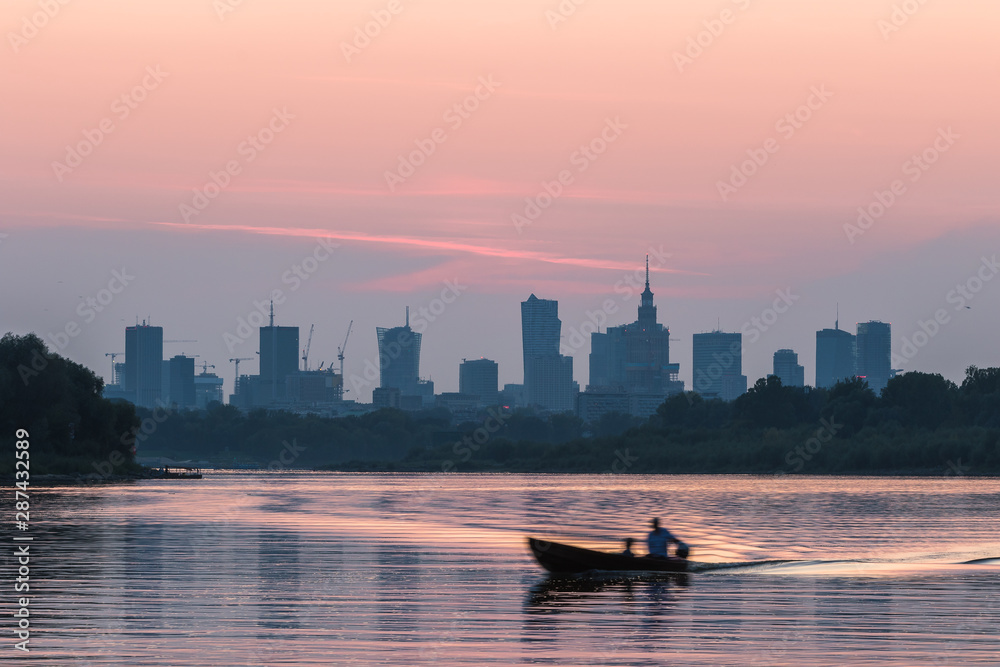Fototapeta premium Colorful Warsaw cityscape with skyscrapers in the downtowan and a boat sailing on the Vistula River during