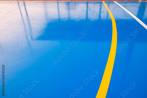 Sports pitch colorful blue field pattern with curved white and yellow touchlines, angled perspective and reflections.