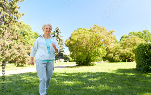 fitness, sport and healthy lifestyle concept - senior woman running or walking along summer park