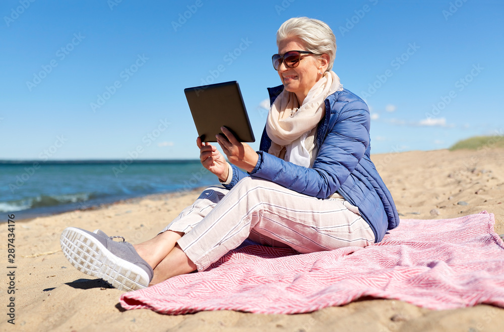 technology, old people and leisure concept - senior woman with tablet computer on beach in estonia