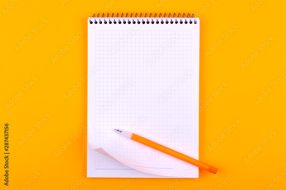 Notebook on a spring with white sheets of paper for drawings, texts and notes, next to a yellow pen lies on an orange background Notebook on a spring with white sheets of paper for drawings, texts and notes, next to a yellow pen lies on an orange background