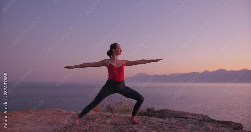 Caucasian woman in red relaxing by practicing yoga on the cliff near calm sea at sunset. Slow motion Caucasian woman in red relaxing by practicing yoga on the cliff near calm sea at sunset. Slow motion