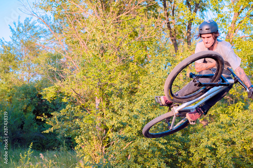 young guy cyclist does jumps and tricks on a bike. in the forest against the setting sun