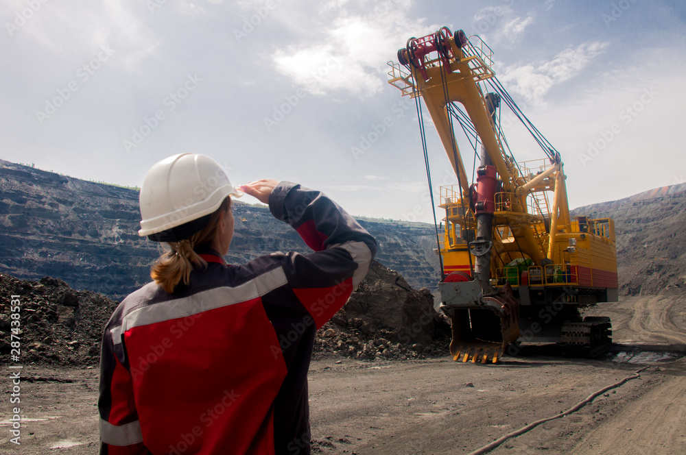 The girl is watching the work of a large excavator in an iron ore quarry.