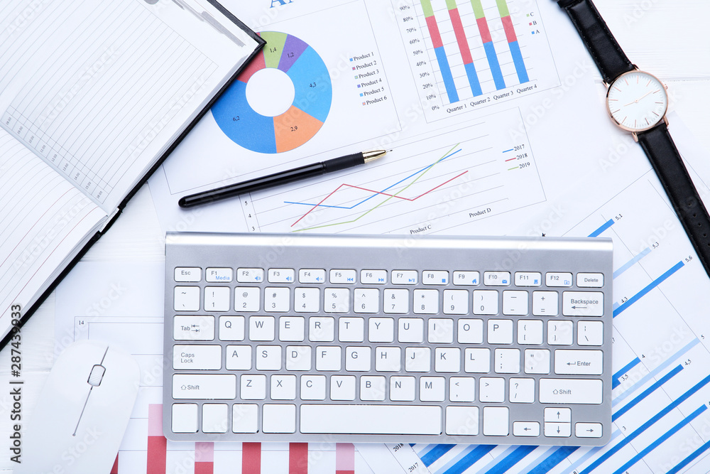 Computer keyboard with diagrams and notepad on white wooden table