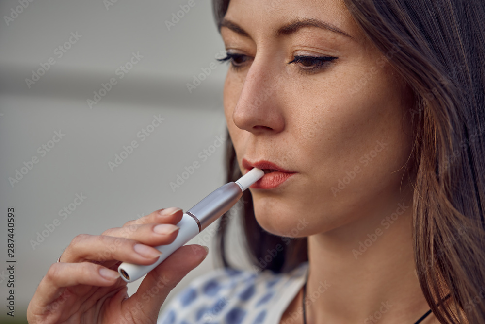 Electronic cigarette technology. Tobacco IQOS system. Close-up of a girl smoking an electric hybrid cigarette with a heating pad. tobacco heating system. Electronic cigarette in female hands.