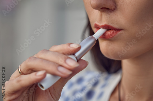 Electronic cigarette technology. Tobacco IQOS system. Close-up of a girl smoking an electric hybrid cigarette with a heating pad. tobacco heating system. Electronic cigarette in female hands.