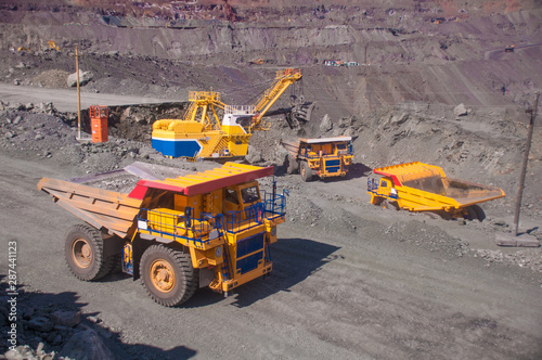 mining machinery works in a quarry. excavator loads a dump truck, heavy trucks transport iron ore. open pit mining