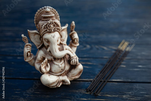 Hindu god Ganesh on black background. Statue on wooden table © Andrii