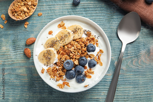 Bowl of yogurt with blueberries, banana and oatmeal on color wooden table, flat lay photo