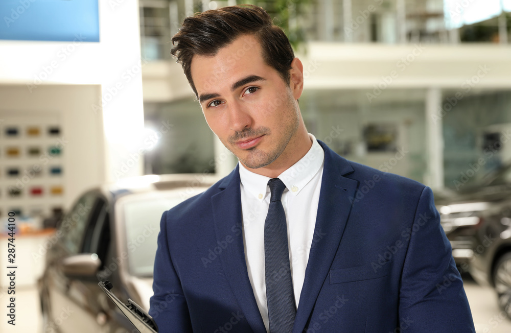 Young salesman with clipboard near car in modern dealership Young salesman with clipboard near car in modern dealership