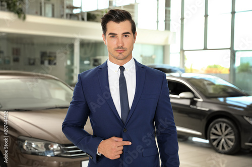 Young salesman near new car in modern dealership © New Africa